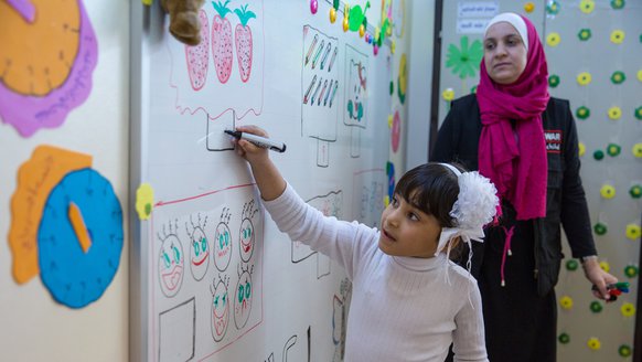 Syrisch meisje tekent op bord in kleuterklas Jordanie - War Child