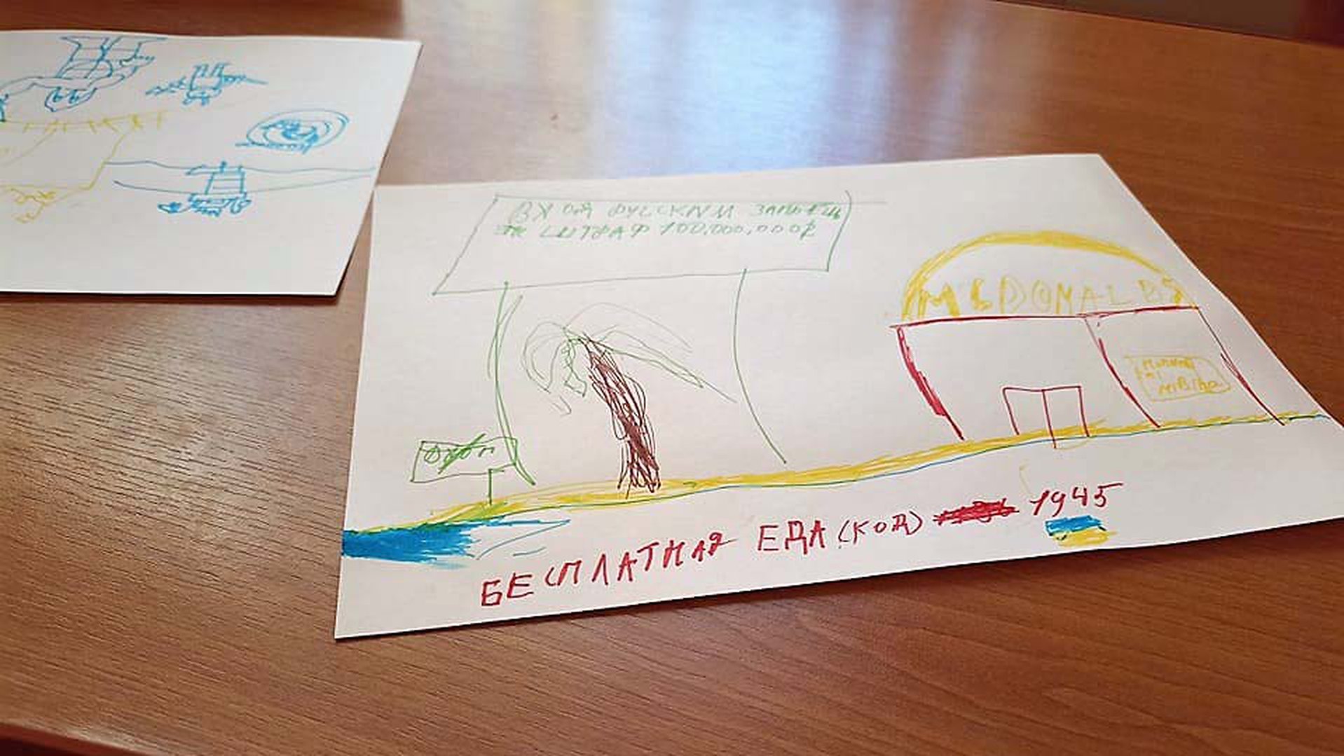 A drawing from a child who fled Ukraine who was asked to draw a house where it feels safe. The drawing is of McDonalds next to a palm tree and water.