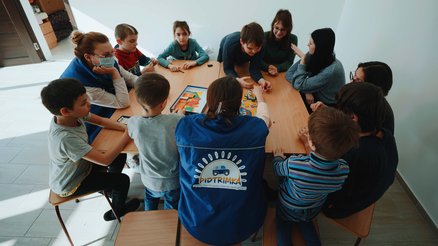 Psychological first aid team plays a game with refugee children from Ukraine around a table.