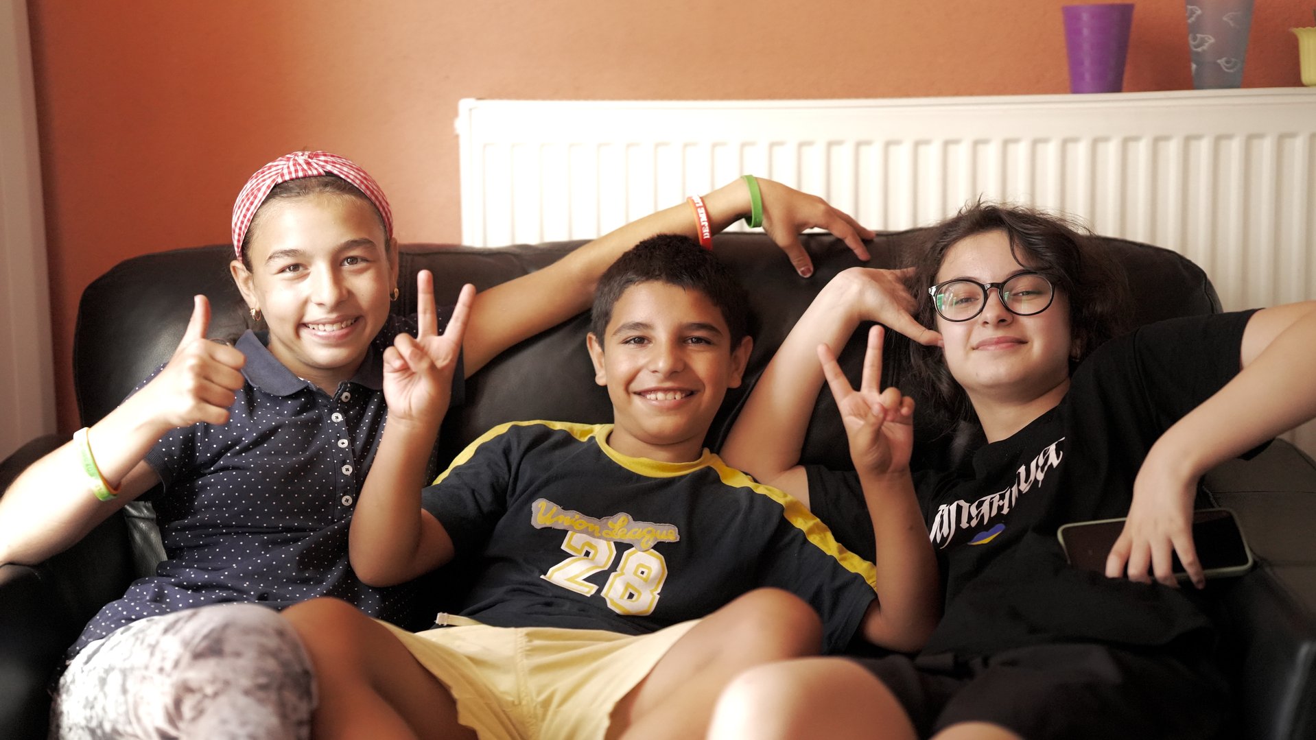 Roda (12) smiling with two friends on a couch in a shelter in Ukraine
